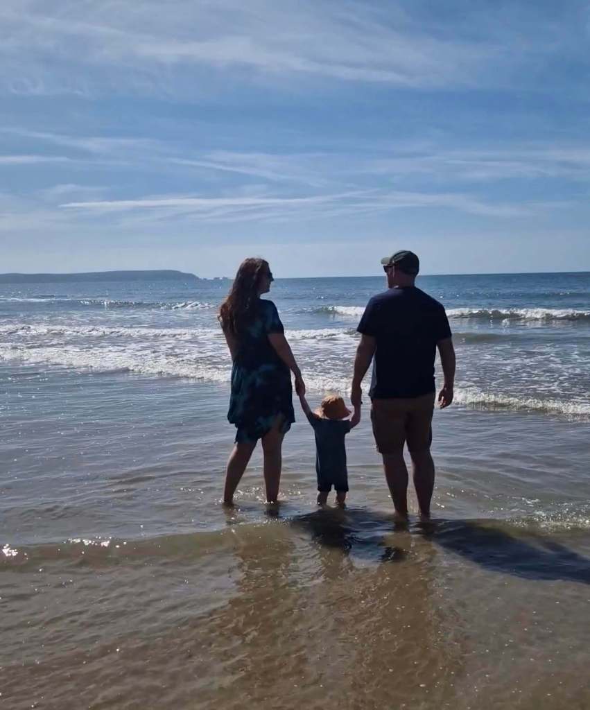 Family of three paddling in the sea with their backs to the camera, symbolising togetherness and a love for slow, meaningful travel