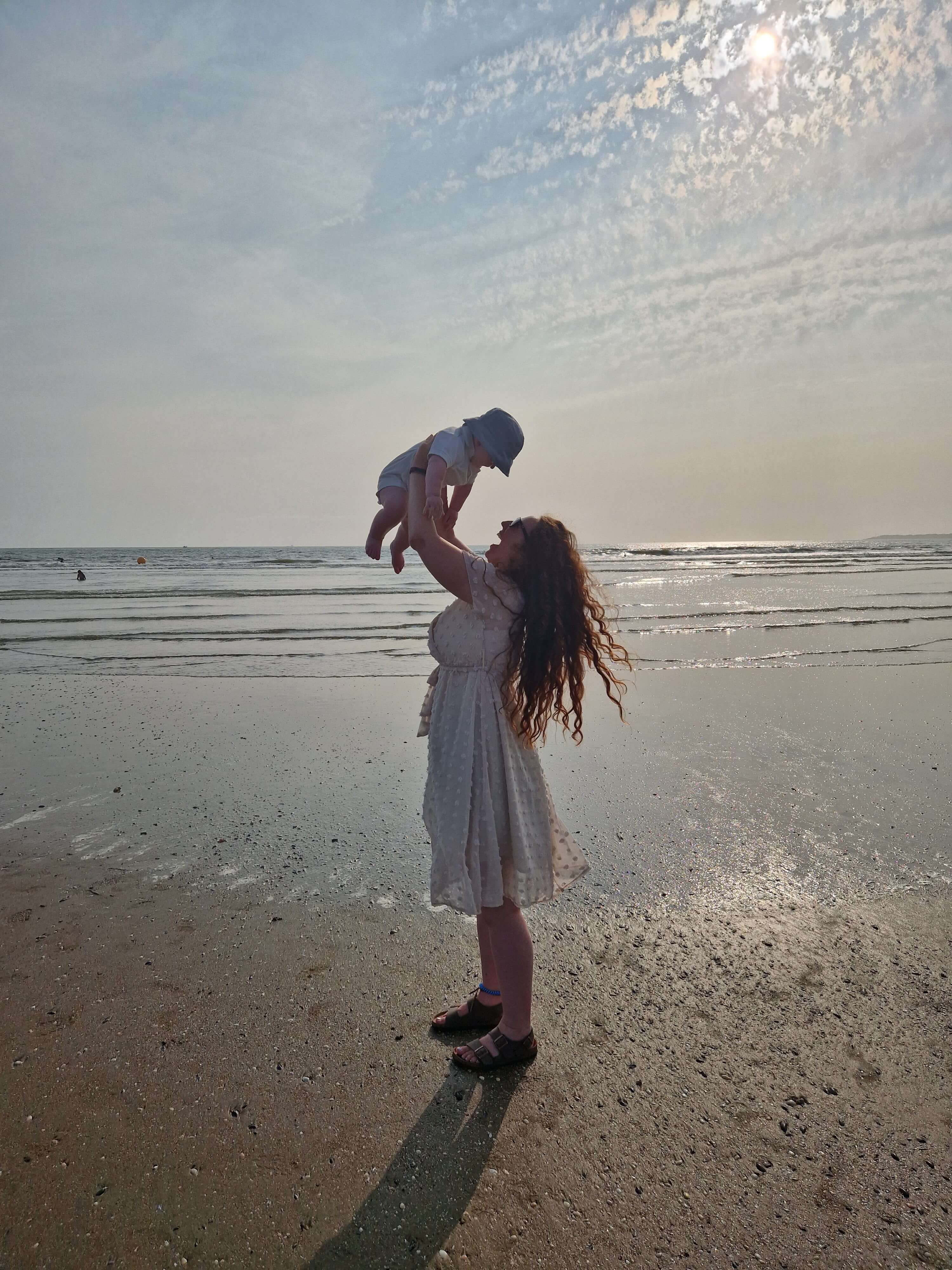 Mother lifting baby into the air on a beach, capturing joy and connection through family travel