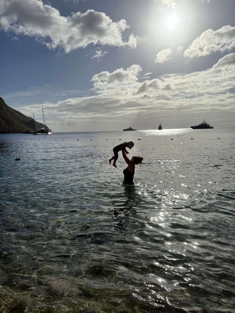 Mum lifting toddler above her head in the clear water at Sugar Beach, Saint Lucia, capturing a joyful family moment.