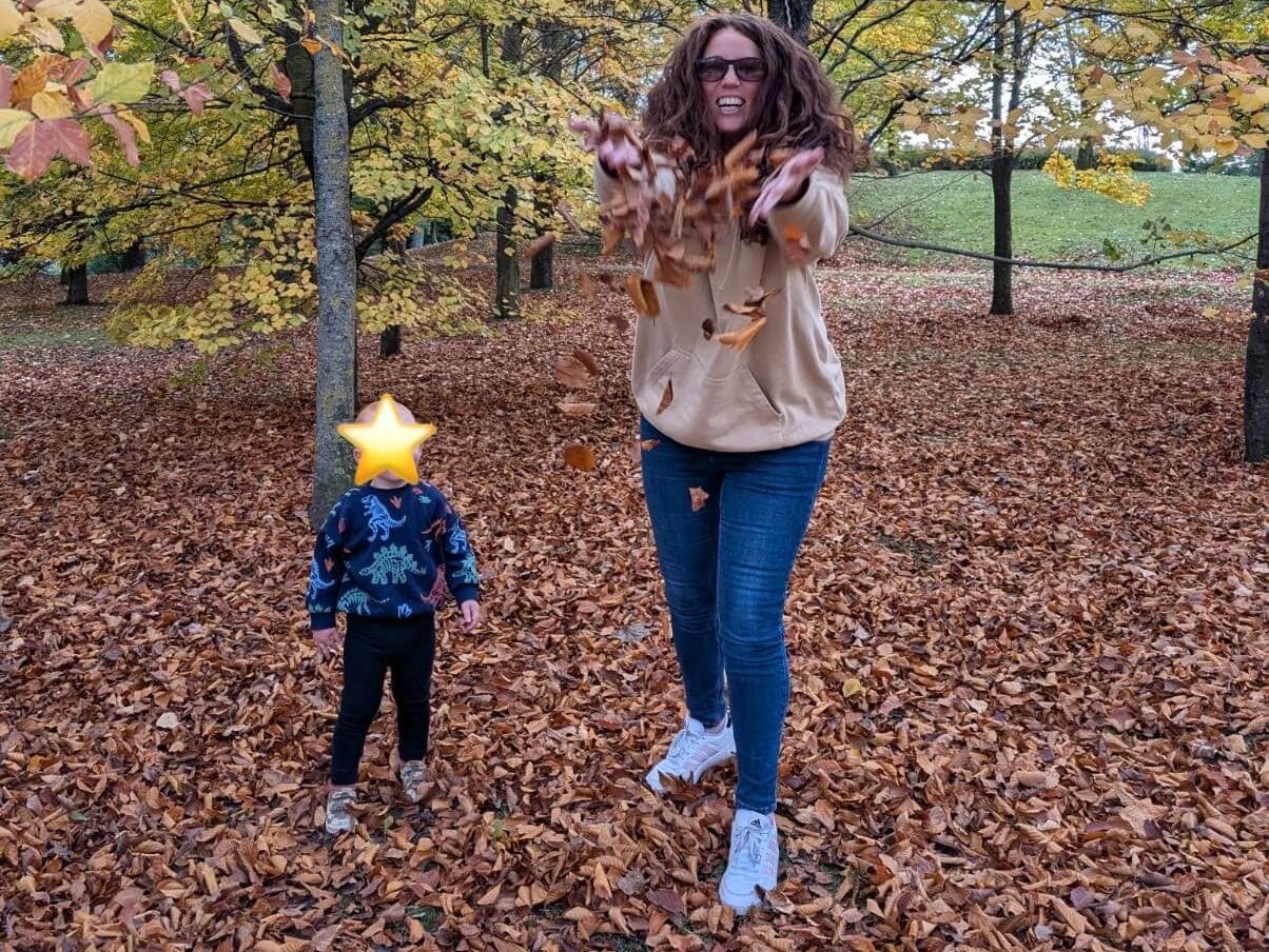 Mother and toddler playing with leaves on land, looking joyful