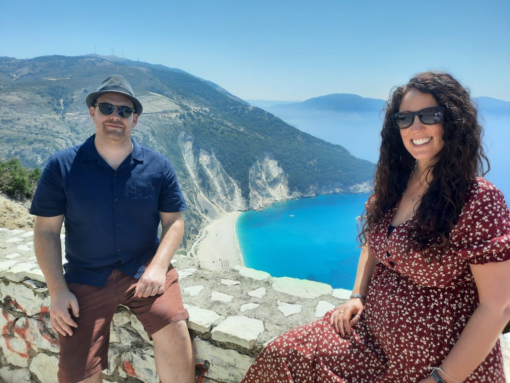 Pregnant couple gazing out at Myrtos Beach from a cliff viewpoint, Kefalonia