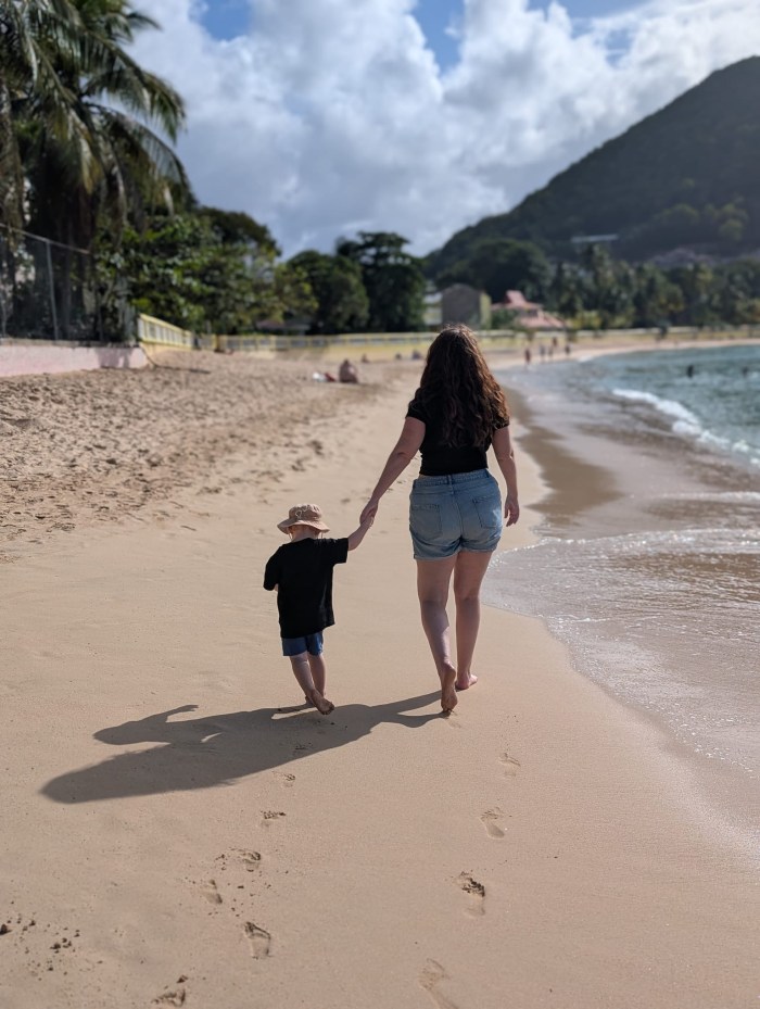Mother walking hand-in-hand with her young son on a sandy beach, backs to the camera
