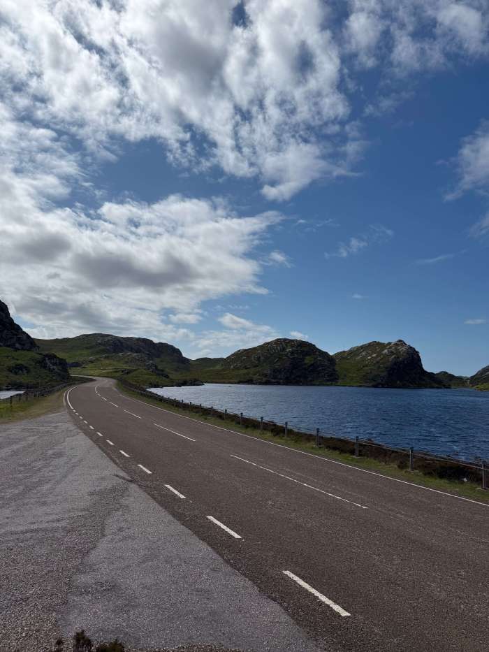 Scenic road trip on the NC500 with a loch to the left and open Highland road ahead