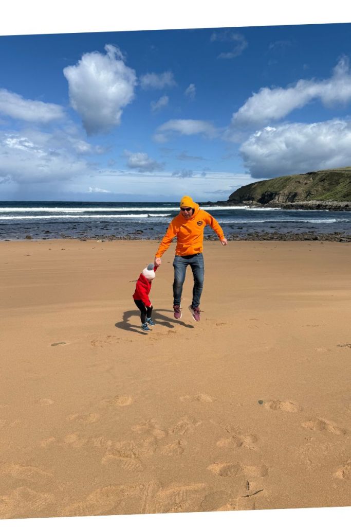Jumping for joy on a chilly NC500 beach day Father and child jumping on a Scottish beach in winter clothing under blue skies