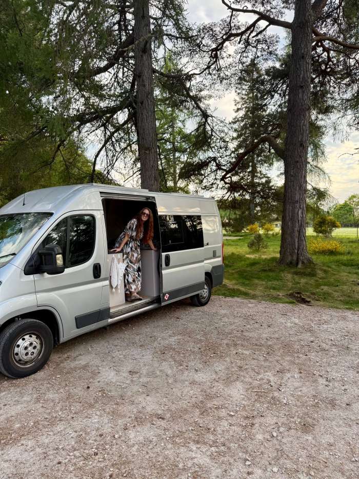 Woman leaning out the side door of a campervan in a forest