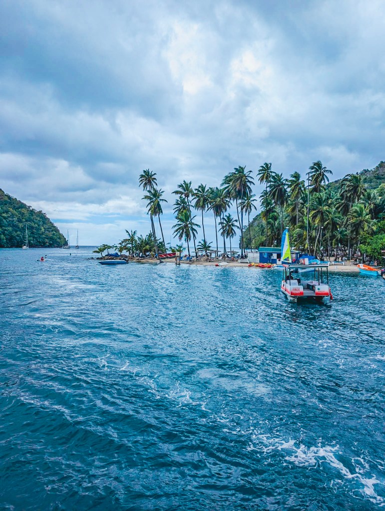 Marigot Bay, Saint Lucia View of Marigot Bay in Saint Lucia with palm trees, a small boat, and a tiny beach seen from the water