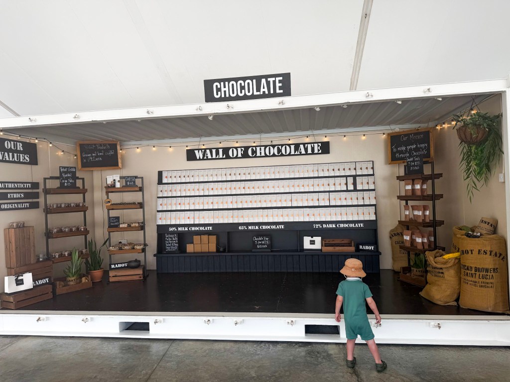 Toddler standing in front of the wall of chocolate bars for sale at Project Chocolat, Rabot Estate, Saint Lucia