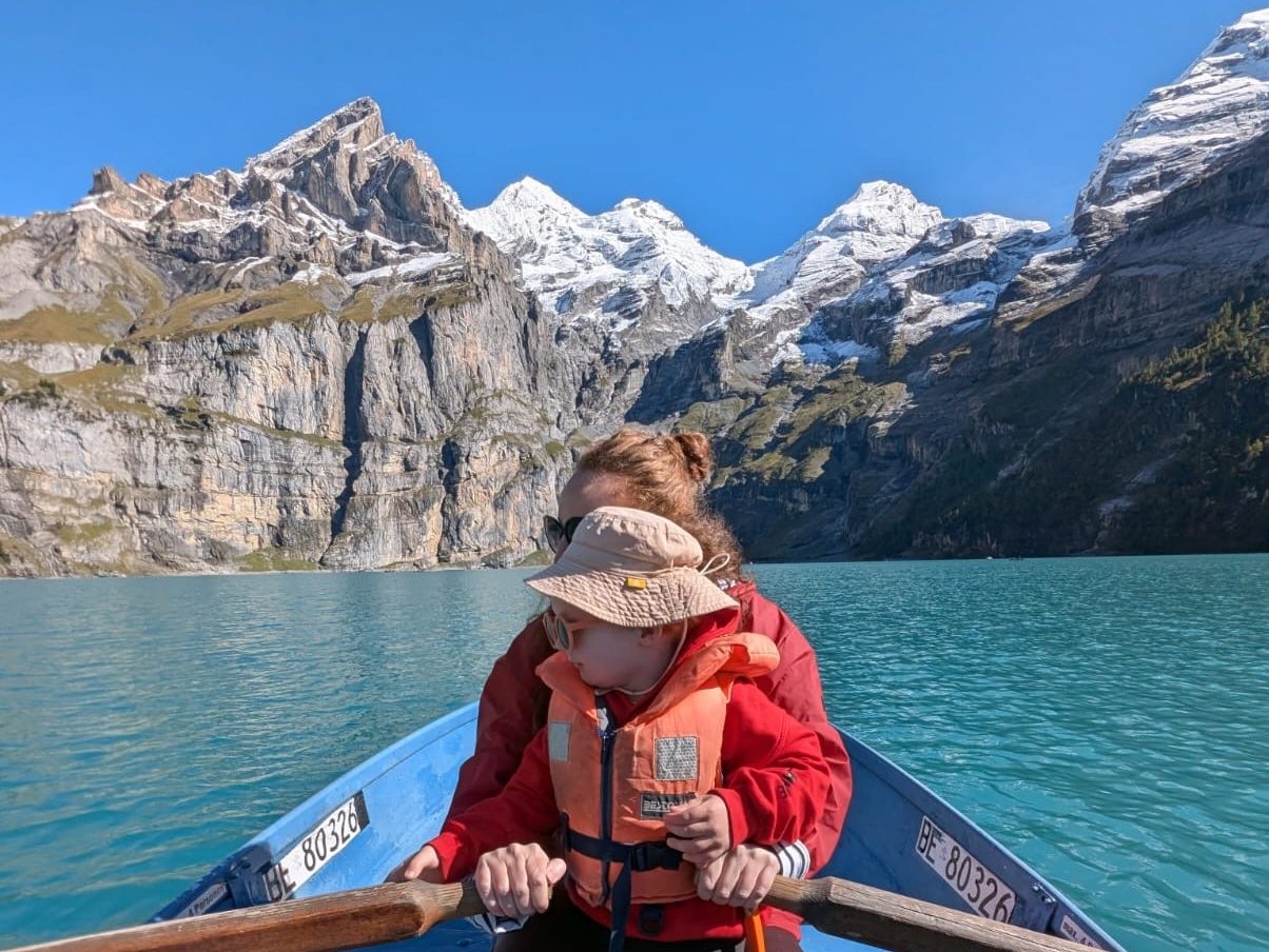 Mother and toddler rowing a boat on turquoise Oeschinensee Lake in Switzerland.