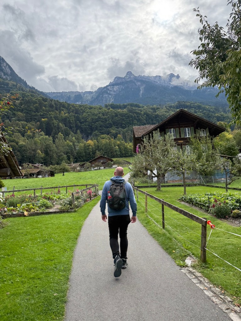 Man walking on a mountain path surrounded by green alpine views in Switzerland.